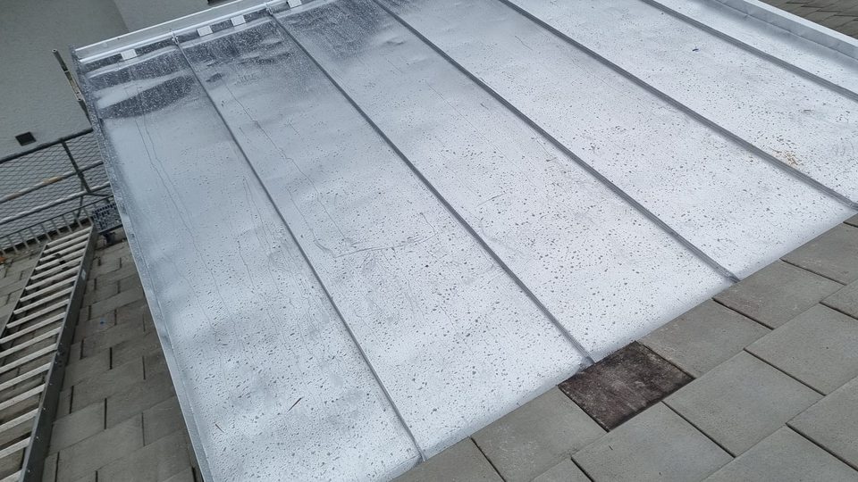 Dachgaube mit Deckung aus Stehfalzblech, daneben die Dachfläche aus Betondachsteinen und ein Gerüst mit Seitenschutz Dachgaube mit Deckung aus Stehfalzblech, daneben die Dachfläche aus Betondachsteinen und ein Gerüst mit Seitenschutz