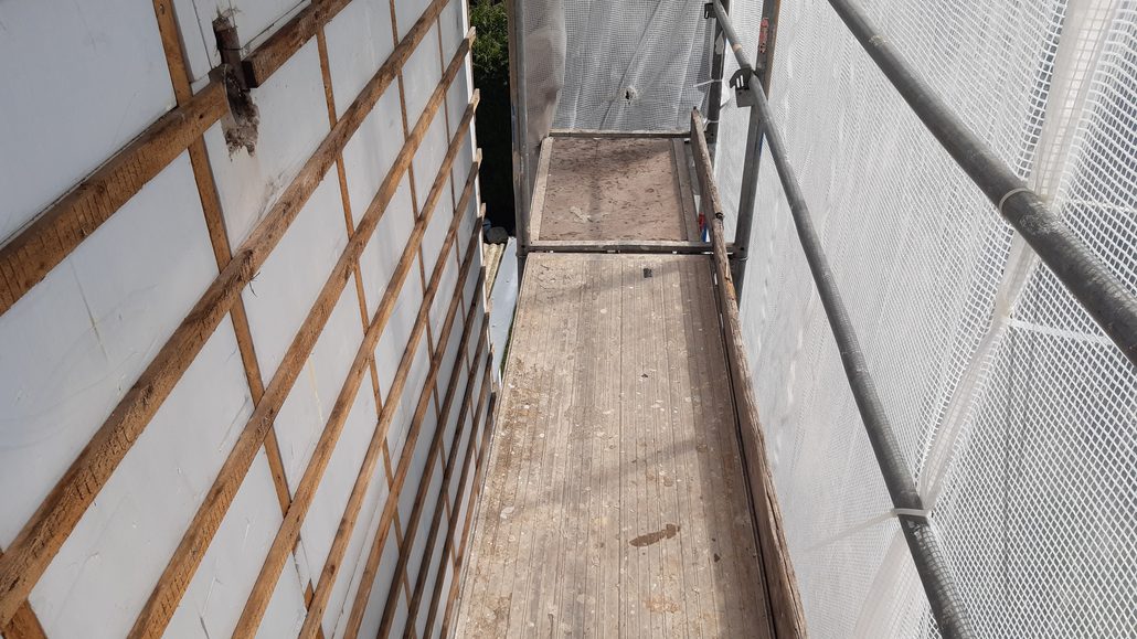 Blick über die Gerüstlage: links die Hauswand mit Dämmplatten und Holzlattung ohne Verkleidung, rechts die Gitterplane Blick über die Gerüstlage: links die Hauswand mit Dämmplatten und Holzlattung ohne Verkleidung, rechts die Gitterplane