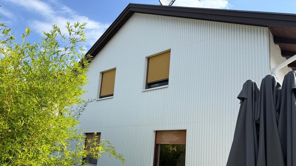 Giebelseite eines Wohnhauses mit neuer heller Fassadenverkleidung aus Wellprofil Giebelseite eines Wohnhauses mit neuer heller Fassadenverkleidung aus Wellprofil